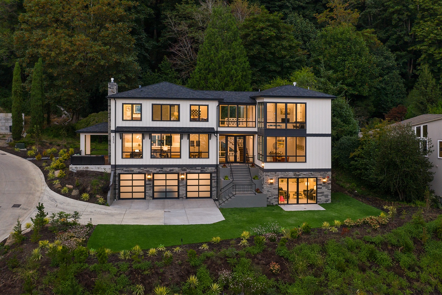 Residence at dusk with white siding, black window frames and landscaped grounds